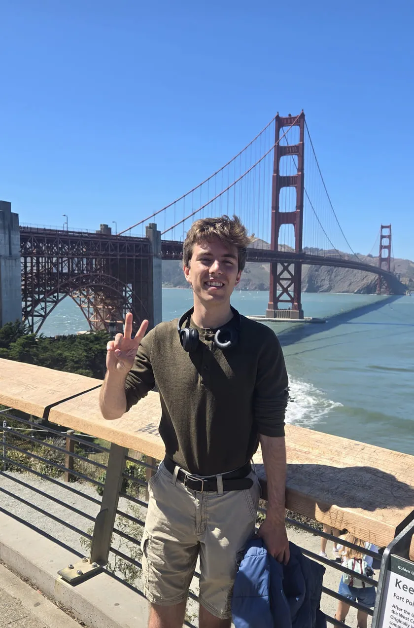 Xander throwing a peace sign in front of the Golden Gate Bridge, headphones around his neck