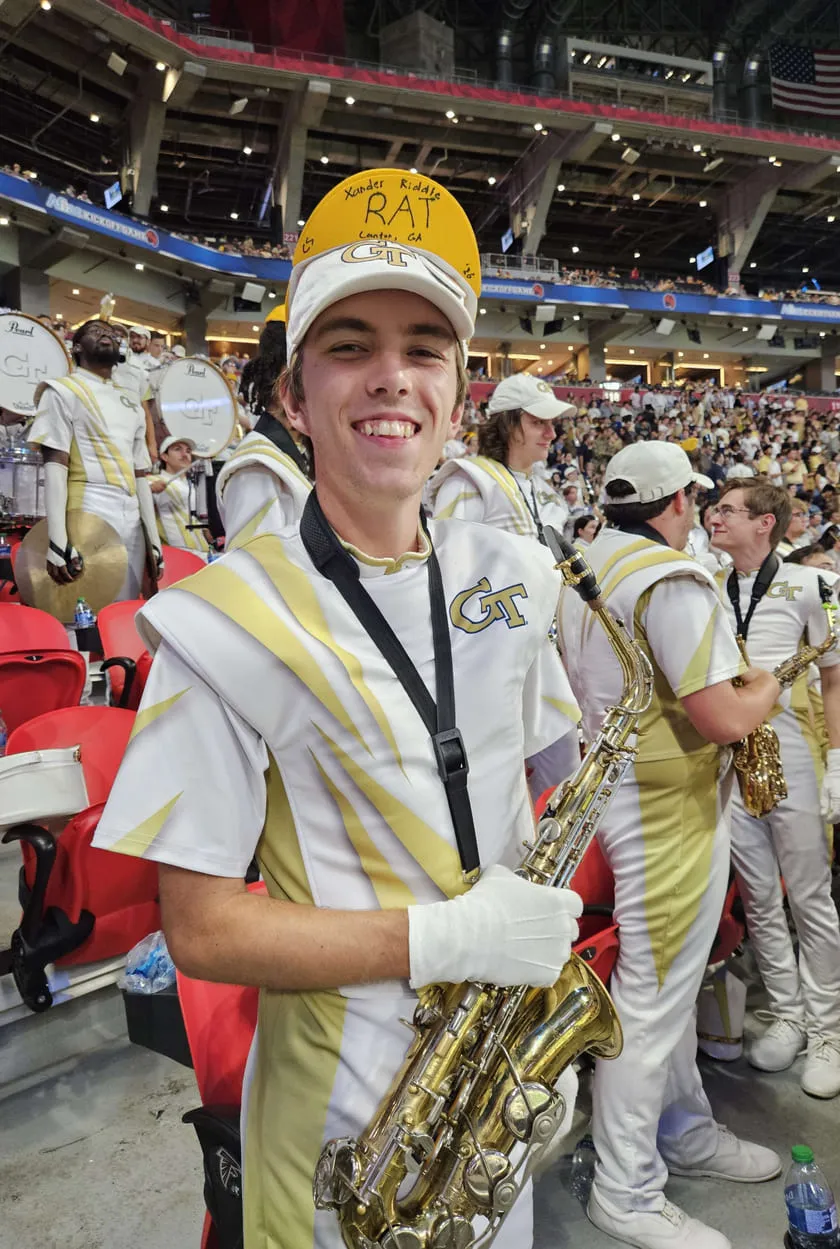 Xander in his Georgia Tech marching band uniform holding a saxophone in the stands